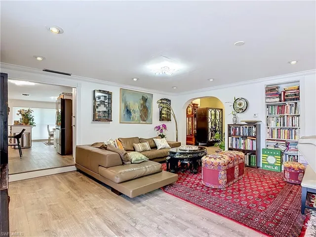 Bright living area featuring recessed lighting, crown molding, built-in shelving, an arched doorway, and wood-finish flooring