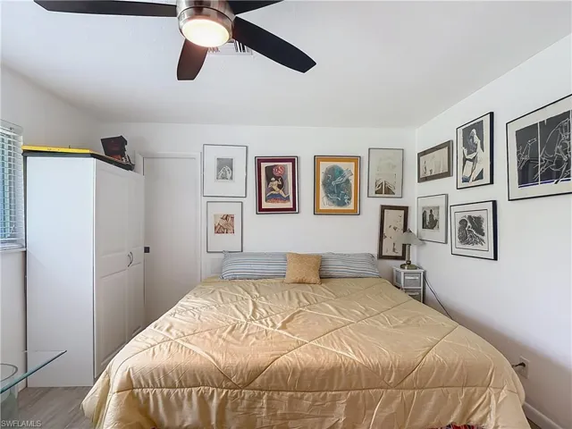 Bedroom with a ceiling fan featuring a brushed nickel fixture and black blades, white walls, and wood-finish flooring