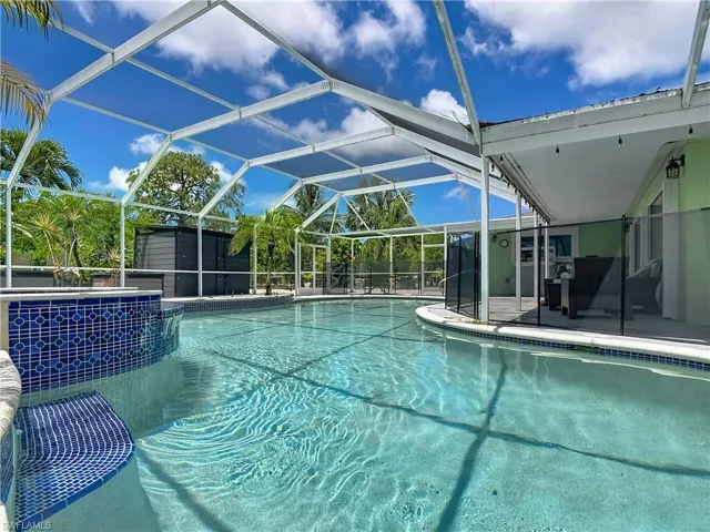 Screened-in pool area featuring a built-in spa with blue mosaic tile, a spacious swimming pool with an integrated seating area, and a covered patio with string lighting