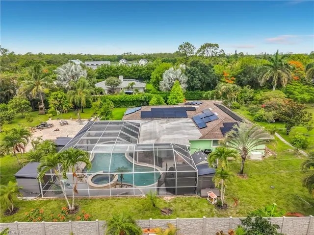 Expansive outdoor living area featuring a caged swimming pool with an integrated spa, surrounded by lush tropical landscaping