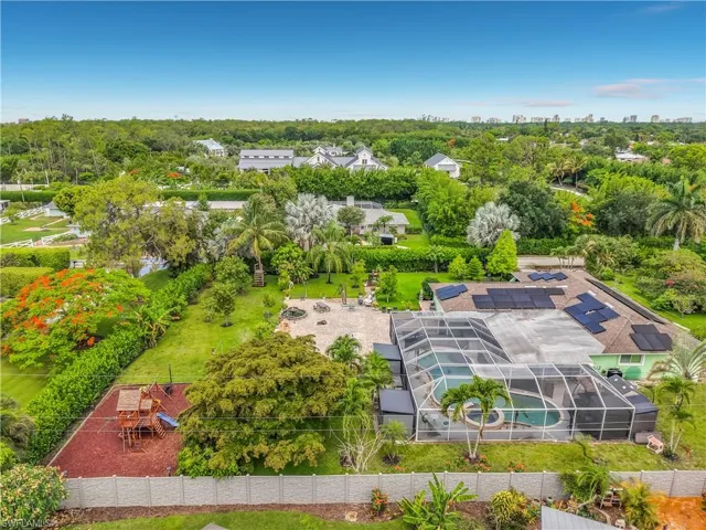 Aerial perspective showcasing the property's expansive grounds, featuring a screened pool enclosure, numerous solar panels, established landscaping, and a fenced recreational area