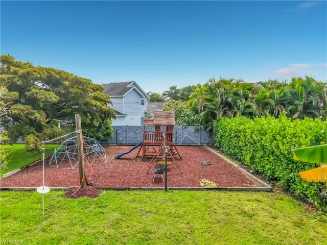 Expansive backyard featuring a dedicated play area with red mulch ground cover, a wooden playset, and a geodesic dome climber
