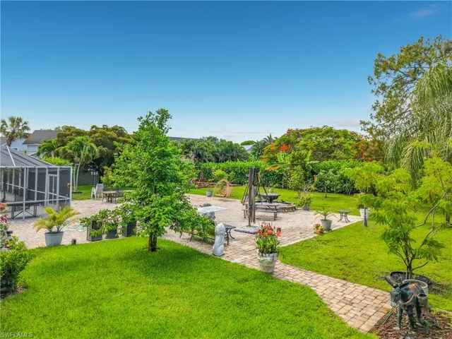 Expansive backyard featuring a screened enclosure, brick paver patio, lush green lawn, mature trees, and flowering shrubs