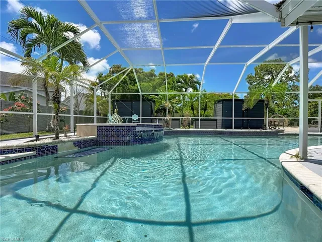 Screened outdoor pool area featuring a built-in spa with blue mosaic tile, integrated steps, and surrounding tropical landscaping