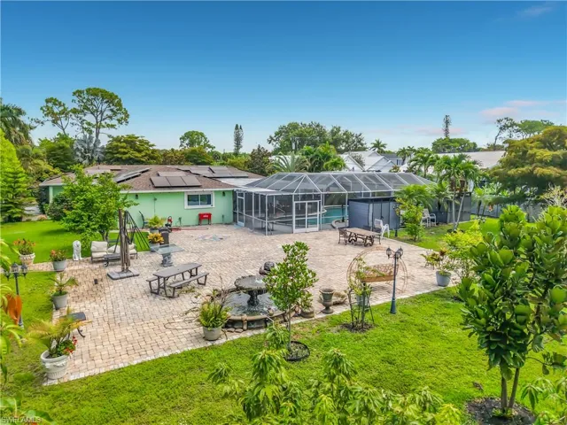 Expansive backyard featuring a large paver patio, screened-in pool enclosure, mature tropical landscaping, and a water fountain feature