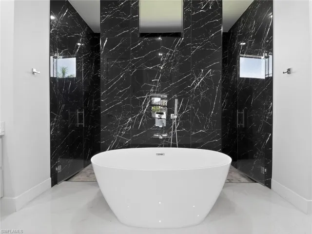 Bathroom featuring stone wall, a soaking tub, a marble finish shower, marble tiled floors, and tile walls