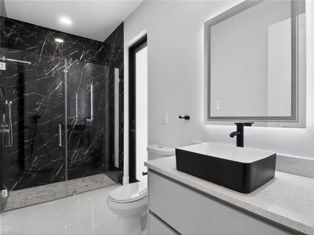 Full bathroom featuring vanity, a marble finish shower, and light marble finish floors