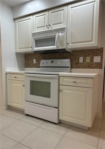Kitchen featuring white appliances, white cabinetry, light tile patterned floors, and decorative backsplash