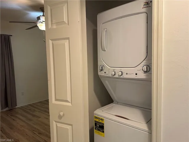 Laundry area featuring dark wood-type flooring, ceiling fan, and stacked washer / dryer
