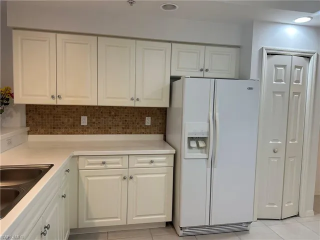 Kitchen with white cabinets, light tile patterned floors, backsplash, and white refrigerator with ice dispenser