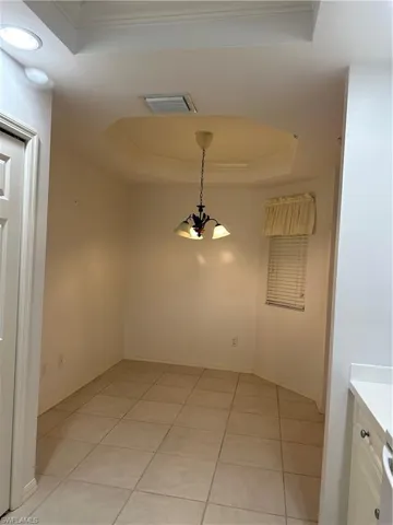 Spare room with crown molding, light tile patterned floors, a raised ceiling, and an inviting chandelier