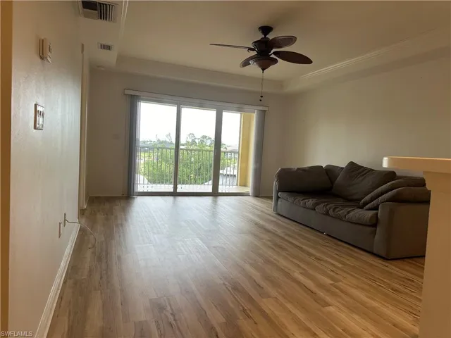 Living room with ceiling fan, light wood-type flooring, crown molding, and a tray ceiling