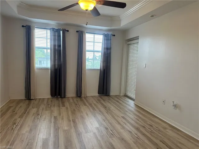 Empty room featuring ceiling fan, a raised ceiling, light wood-type flooring, and ornamental molding