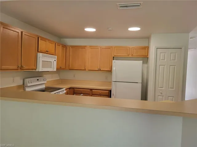 Kitchen featuring white appliances, light countertops, recessed lighting, and a peninsula