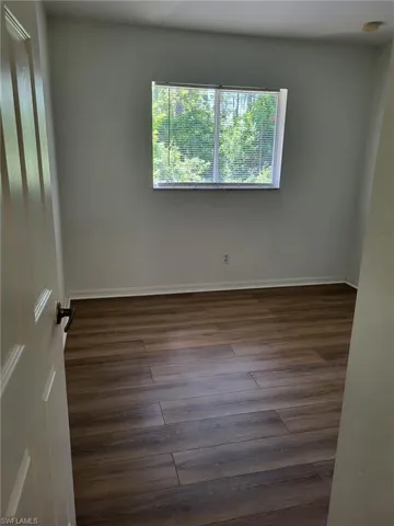 Spare room featuring dark wood-style flooring and baseboards
