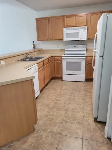 Kitchen featuring white appliances, a peninsula, light countertops, and light tile patterned flooring