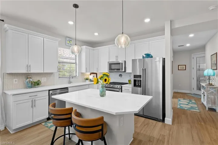 Kitchen with high end appliances, light wood-style floors, white cabinets, tasteful backsplash, and recessed lighting