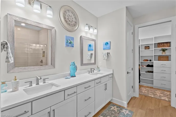 Full bath featuring a spacious closet, double vanity, light wood-style floors, and a shower stall