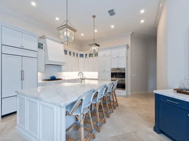 Kitchen with an island with sink, custom range hood, stainless steel double oven, and Quartzite countertops