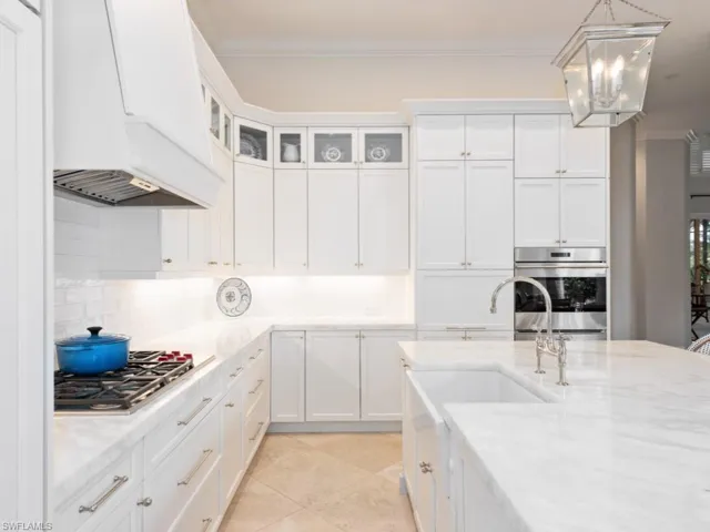 Kitchen featuring stainless steel appliances, premium range hood, white cabinets, decorative light fixtures, and backsplash