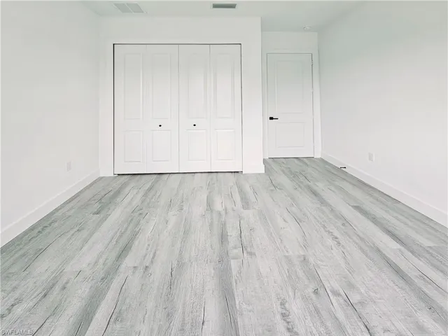 Unfurnished bedroom with wood finished floors, baseboards, a closet, and visible vents