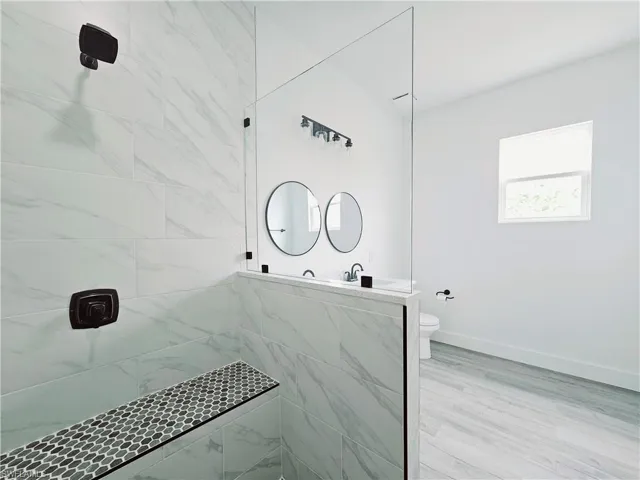 Full bath with baseboards, toilet, and tiled shower