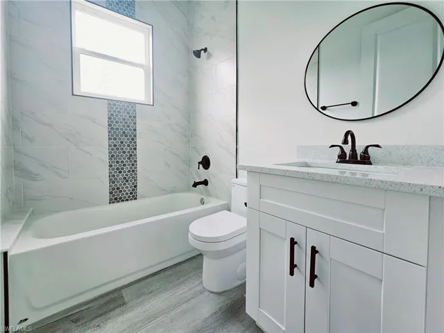 Full bathroom featuring toilet, vanity, washtub / shower combination, and wood finished floors