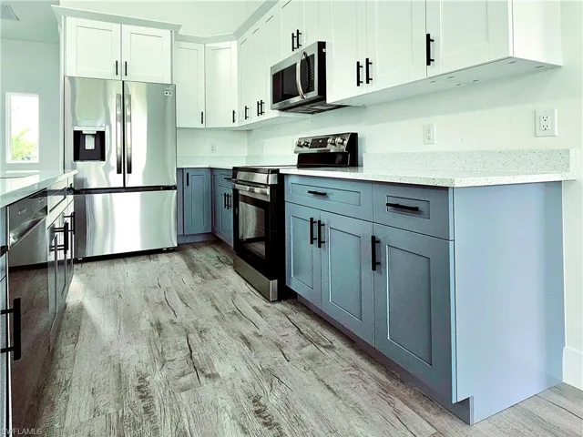 Kitchen featuring white cabinetry, light stone countertops, appliances with stainless steel finishes, gray cabinetry, and light wood-style flooring