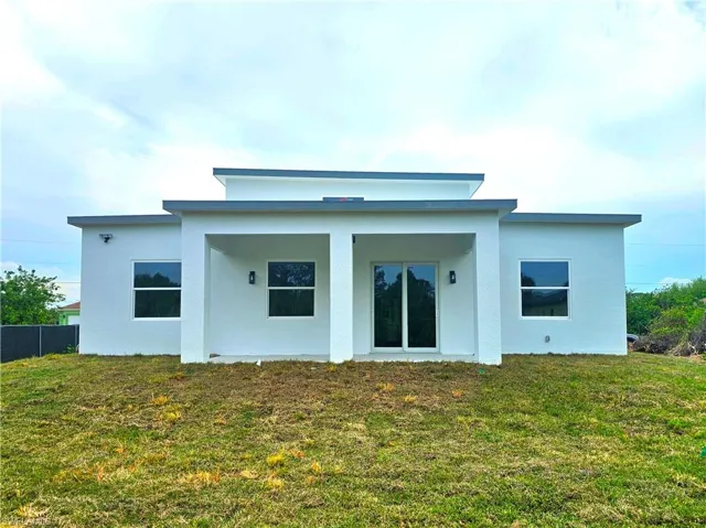 Rear view of house featuring a lawn, fence, and stucco siding