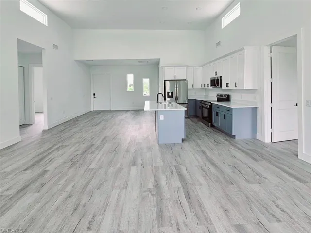 Kitchen with open floor plan, light countertops, stainless steel appliances, a towering ceiling, and white cabinets