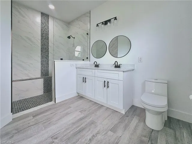 Bathroom with toilet, a walk in shower, vanity, wood finished floors, and baseboards