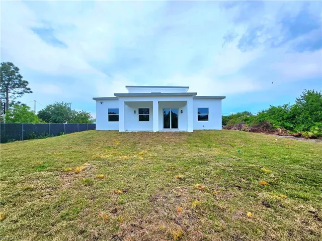 Rear view of property with stucco siding, fence, and a lawn
