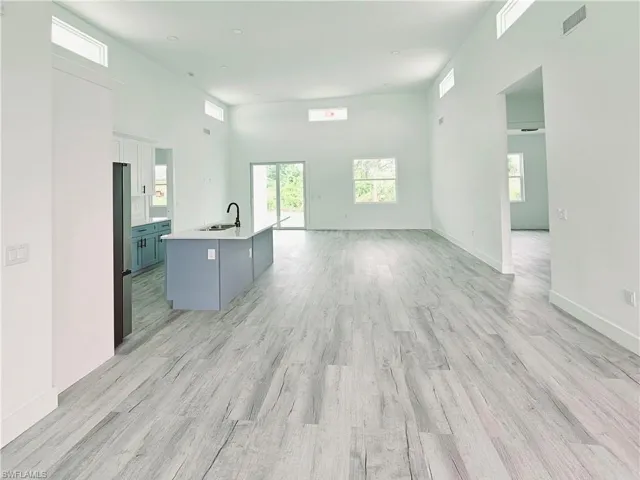 Unfurnished living room featuring visible vents, baseboards, a sink, light wood-style floors, and a high ceiling