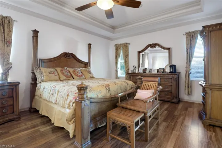 Bedroom with a tray ceiling, crown molding, dark wood finished floors, and ceiling fan