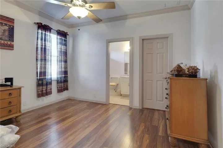 Bedroom featuring crown molding, dark wood-style flooring, ceiling fan, and ensuite bath