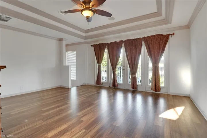 Empty room with plenty of natural light, a tray ceiling, ornamental molding, ceiling fan, and wood finished floors