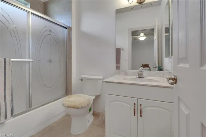 Full bath featuring shower / bath combination with glass door, vanity, light tile patterned floors, and a ceiling fan