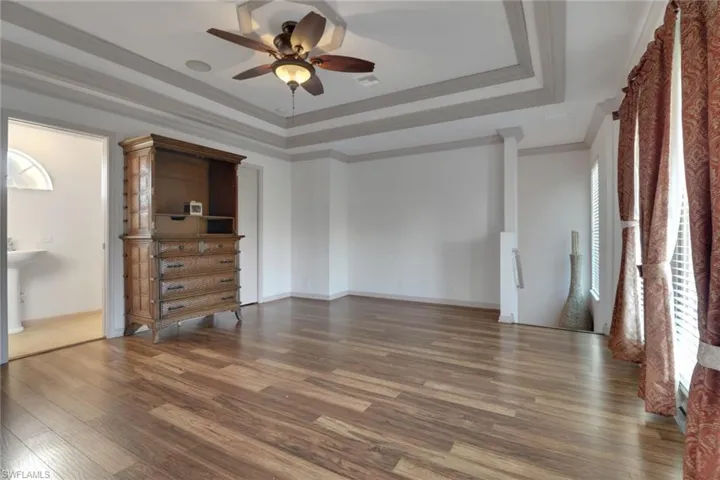 Unfurnished bedroom with a raised ceiling, wood finished floors, crown molding, and a ceiling fan
