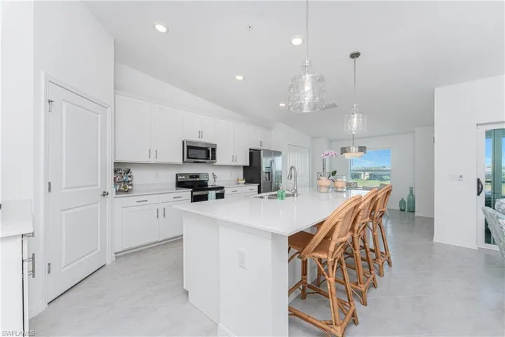 Kitchen with a kitchen bar, a center island with sink, lofted ceiling, white cabinetry, and decorative light fixtures