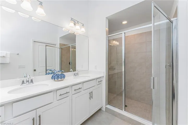 Full bath featuring double vanity, a stall shower, and light tile patterned flooring