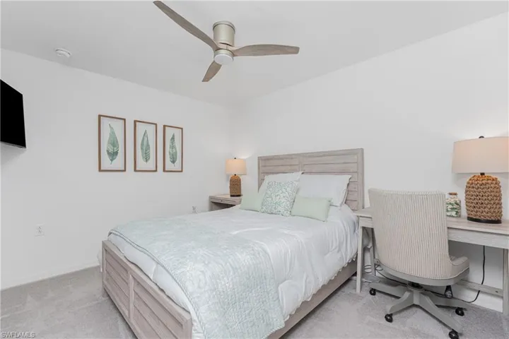 Bedroom featuring light carpet, a ceiling fan, and a desk
