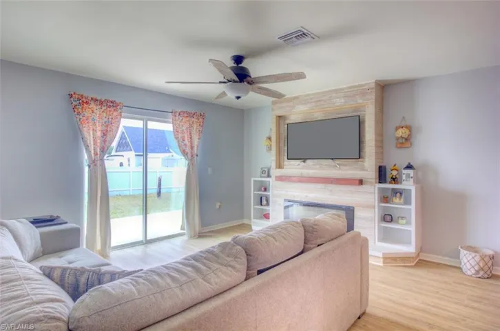 Living room featuring a large fireplace, visible vents, baseboards, a ceiling fan, and light wood-type flooring