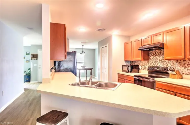 Kitchen with under cabinet range hood, a breakfast bar, backsplash, a sink, and black appliances