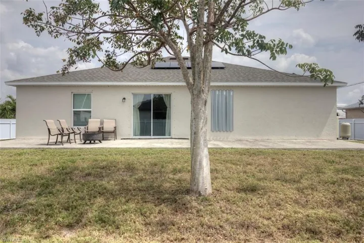 Rear view of property with stucco siding, roof mounted solar panels, a shingled roof, a patio, and a lawn