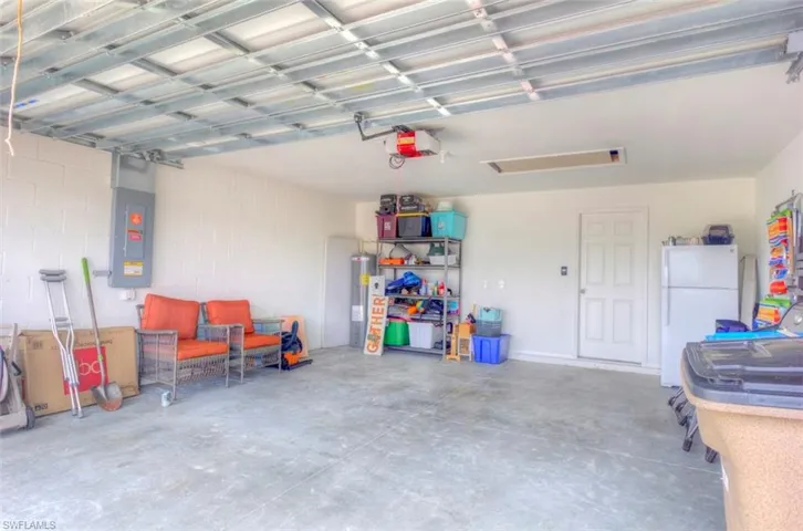 Garage featuring electric panel, a garage door opener, electric water heater, and freestanding refrigerator