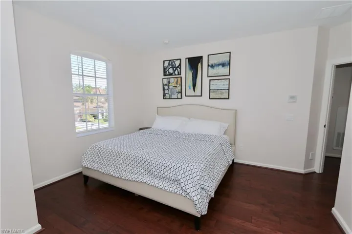 Bedroom featuring wood-finish flooring, an arched window with blinds, and light-toned walls