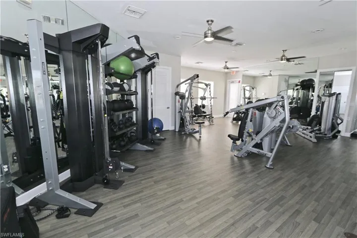 Fitness center featuring wood-finish flooring, mirrored walls, and multiple ceiling fans
