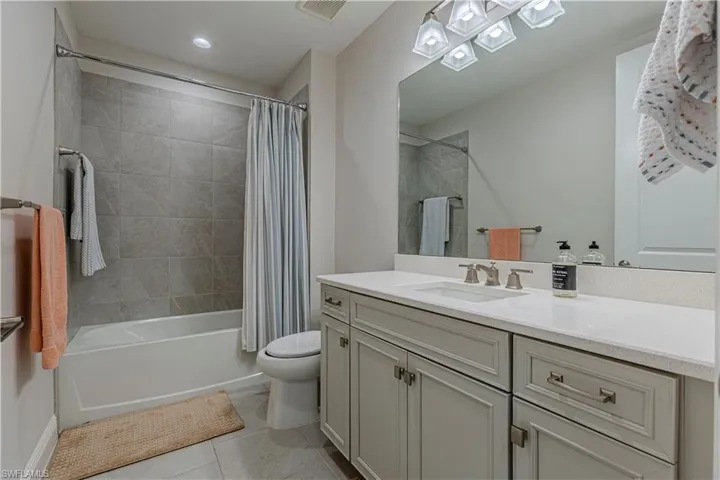 Bathroom w/ vanity, light tile patterned floors, and shower / bathtub combination w/ curtain