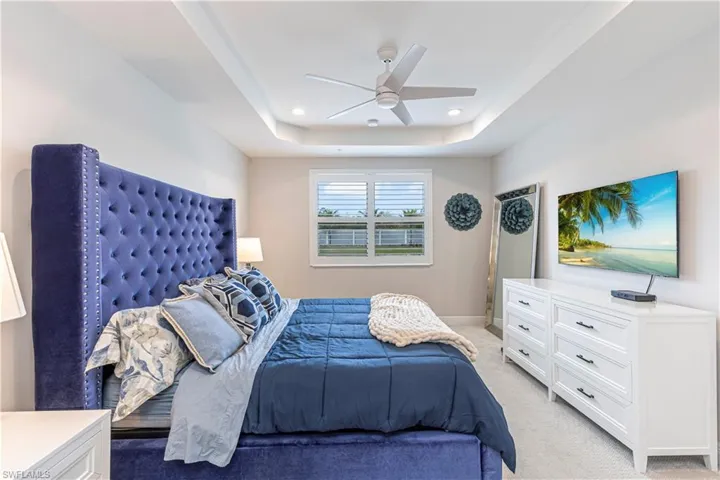 Bedroom w/ light colored carpet, tray ceiling, ceiling fan & recessed lighting