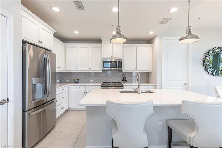 Kitchen featuring stainless steel appliances, white cabinets, breakfast bar & island w/ sink